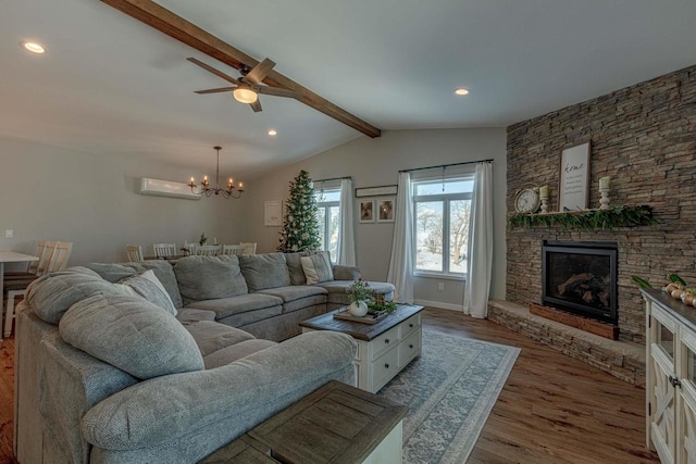 living room with ceiling fan with notable chandelier, a wall unit AC, wood-type flooring, lofted ceiling with beams, and a stone fireplace