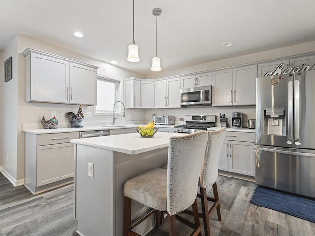 kitchen featuring stainless steel appliances, sink, wood-type flooring, a kitchen island, and hanging light fixtures