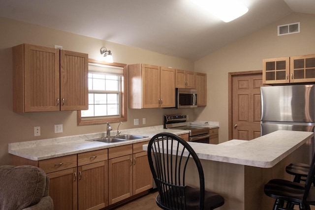 kitchen featuring lofted ceiling, sink, appliances with stainless steel finishes, a kitchen island, and a breakfast bar area