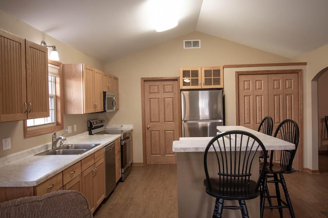 kitchen with a breakfast bar, lofted ceiling, sink, appliances with stainless steel finishes, and wood-type flooring