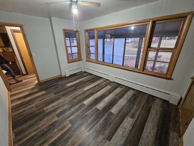 unfurnished room featuring ceiling fan, wood walls, dark wood-type flooring, and a baseboard radiator