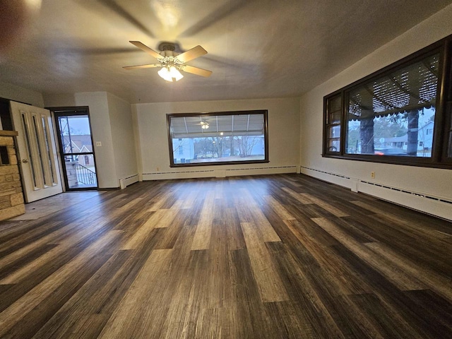 unfurnished living room with a wealth of natural light, ceiling fan, dark hardwood / wood-style floors, and a baseboard heating unit