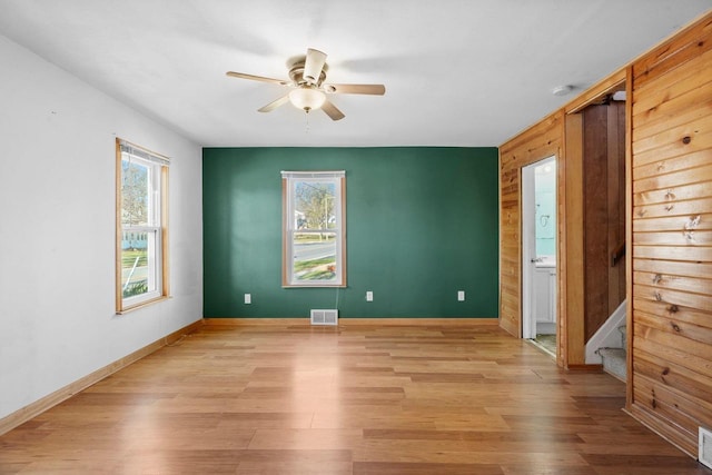 unfurnished room with light wood-type flooring, ceiling fan, and wooden walls