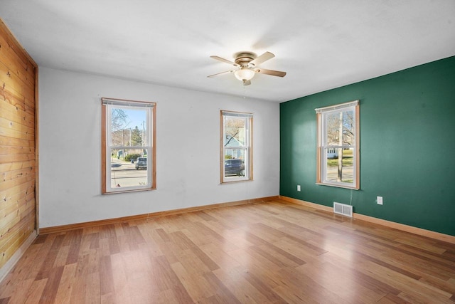 empty room with light hardwood / wood-style flooring, ceiling fan, and wood walls