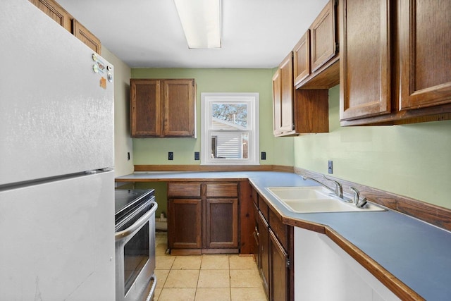 kitchen featuring white refrigerator, light tile patterned floors, sink, and stainless steel stove