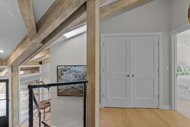 hall with lofted ceiling with skylight and light hardwood / wood-style flooring