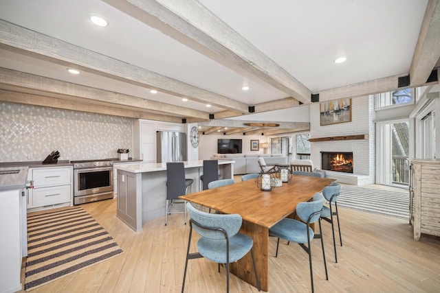 dining area with beamed ceiling, light hardwood / wood-style floors, and a brick fireplace