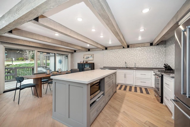 kitchen with light hardwood / wood-style flooring, appliances with stainless steel finishes, beamed ceiling, a kitchen island, and white cabinetry