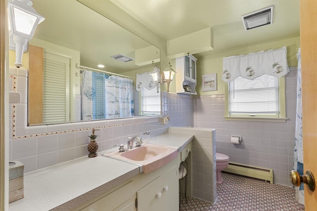 bathroom with vanity, baseboard heating, a healthy amount of sunlight, and tile walls