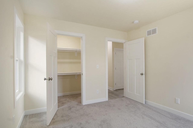 unfurnished bedroom with light carpet, a walk in closet, and a closet