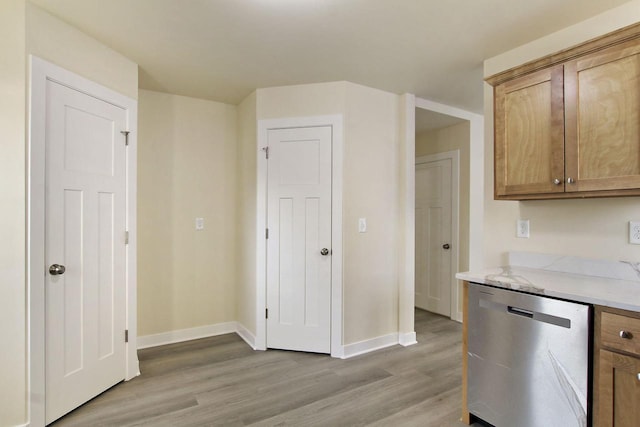 kitchen with light stone counters, stainless steel dishwasher, and light wood-type flooring