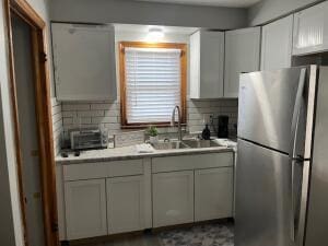 kitchen with backsplash, stainless steel refrigerator, white cabinetry, and sink