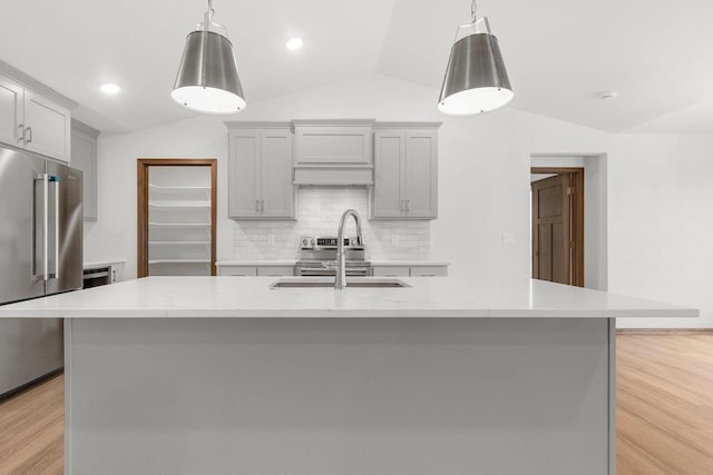 kitchen with pendant lighting, a large island with sink, light stone countertops, light wood-type flooring, and high end fridge