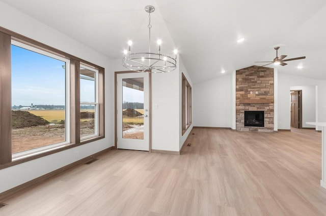 unfurnished living room featuring a stone fireplace, ceiling fan with notable chandelier, light hardwood / wood-style floors, and lofted ceiling