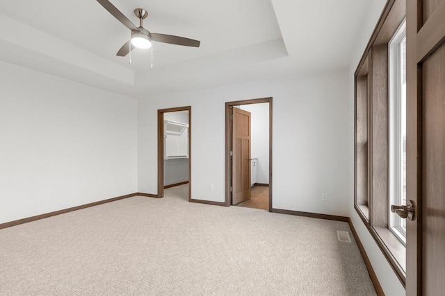 unfurnished bedroom featuring ensuite bathroom, a raised ceiling, ceiling fan, light colored carpet, and a closet