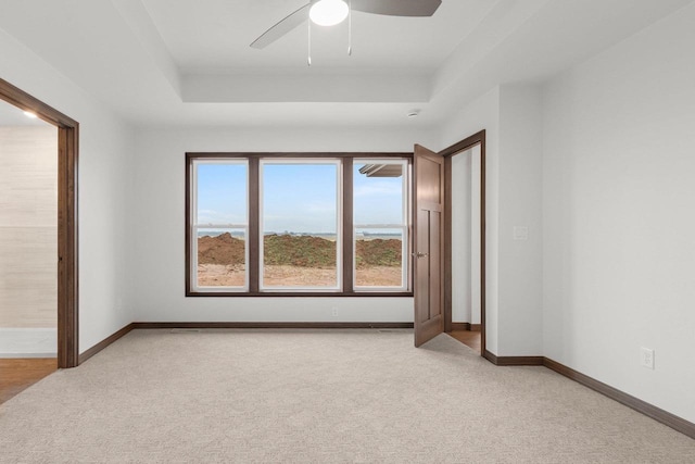 carpeted spare room with ceiling fan and a tray ceiling