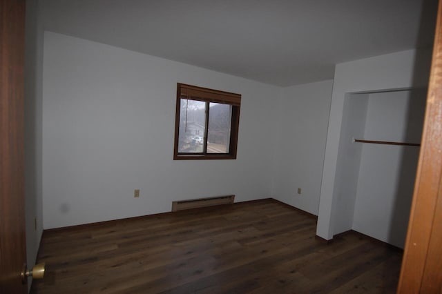 unfurnished bedroom with baseboard heating and dark hardwood / wood-style floors