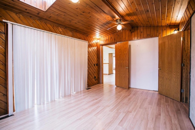 spare room featuring lofted ceiling with skylight, light hardwood / wood-style flooring, wooden walls, and wooden ceiling