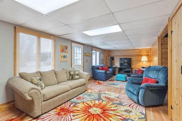 living room with wood-type flooring, a wood stove, a drop ceiling, and wood walls