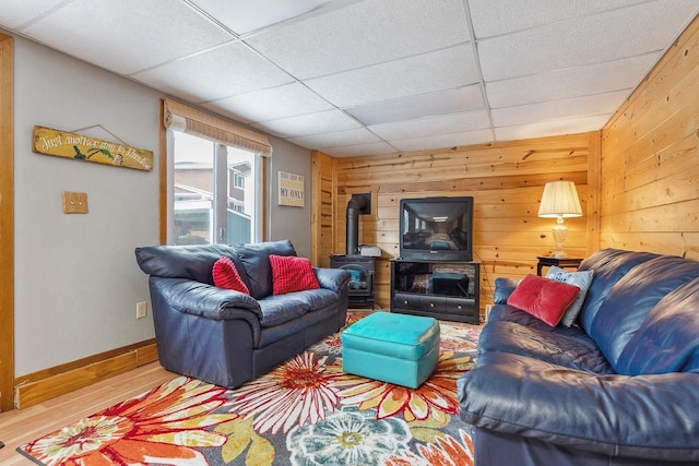 living room featuring hardwood / wood-style floors, a paneled ceiling, a wood stove, and wood walls