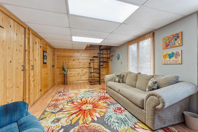 living room with a paneled ceiling, wood walls, and light wood-type flooring