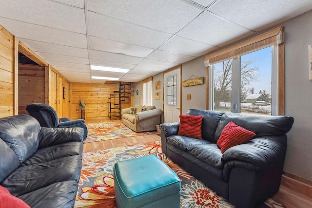 living room featuring wood-type flooring, a drop ceiling, and wooden walls