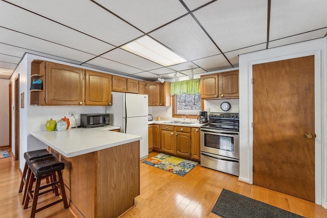 kitchen with stainless steel electric range, a kitchen breakfast bar, light hardwood / wood-style floors, white fridge, and kitchen peninsula