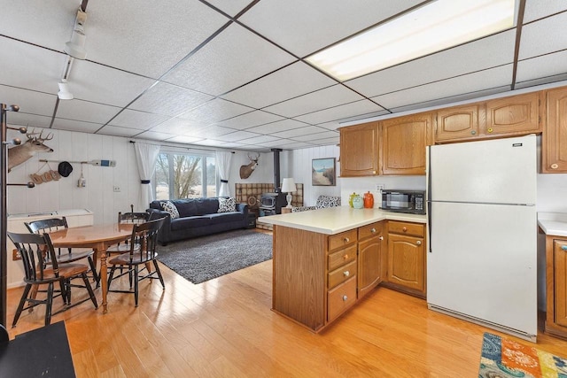 kitchen with kitchen peninsula, light wood-type flooring, a paneled ceiling, white refrigerator, and a wood stove