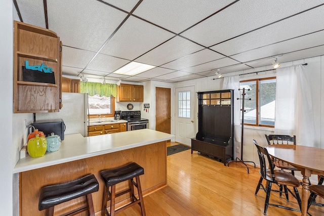 kitchen with stainless steel electric stove, a kitchen breakfast bar, white refrigerator, light hardwood / wood-style flooring, and kitchen peninsula