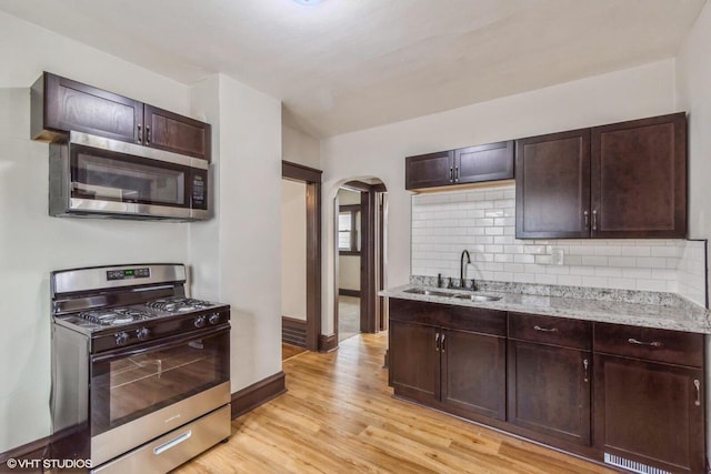 kitchen with sink, dark brown cabinets, light hardwood / wood-style floors, light stone counters, and stainless steel appliances