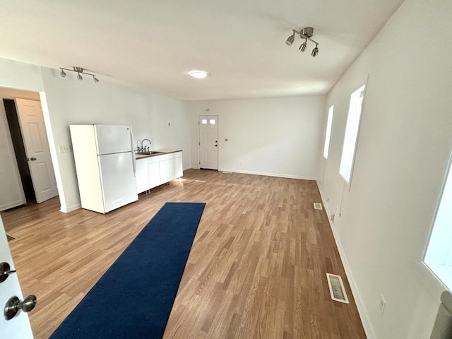 interior space with white refrigerator, light wood-type flooring, sink, and white cabinetry