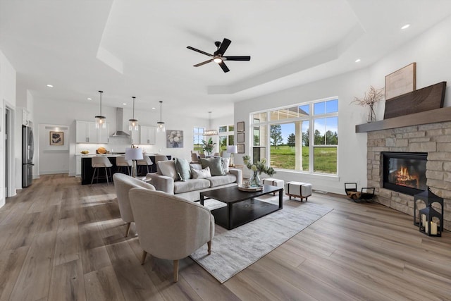 living room with hardwood / wood-style floors, a tray ceiling, a stone fireplace, and ceiling fan