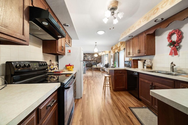 kitchen with sink, black appliances, pendant lighting, light hardwood / wood-style floors, and range hood