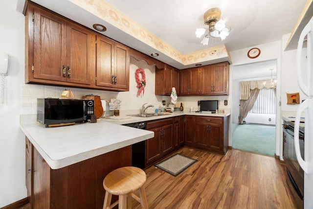 kitchen featuring kitchen peninsula, a breakfast bar, black appliances, light hardwood / wood-style flooring, and a notable chandelier