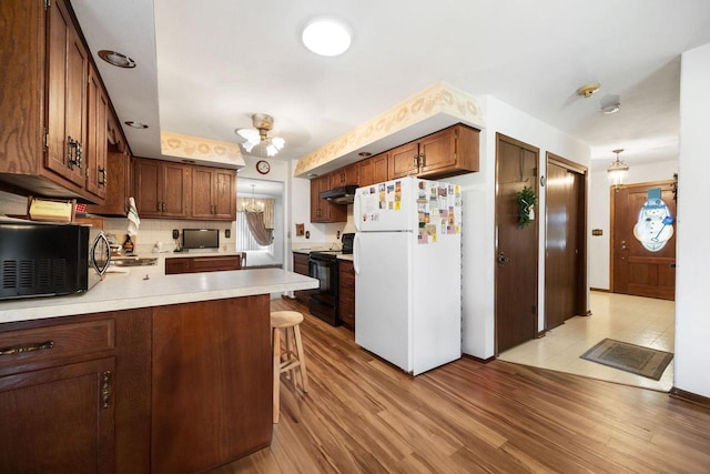 kitchen with backsplash, kitchen peninsula, light hardwood / wood-style floors, a breakfast bar area, and black appliances