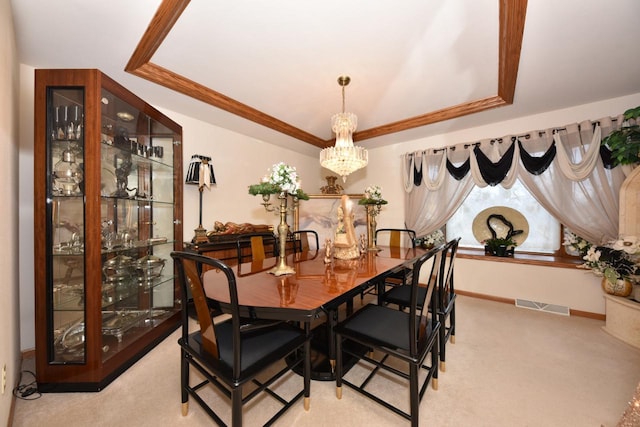 dining room with light carpet, a raised ceiling, ornamental molding, and a notable chandelier