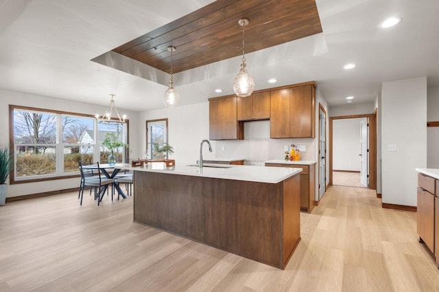 kitchen with a kitchen island with sink, light hardwood / wood-style floors, a raised ceiling, and decorative light fixtures