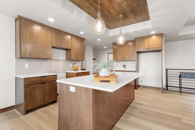 kitchen with light wood-type flooring, backsplash, a tray ceiling, and a center island with sink