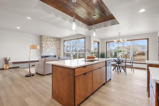 kitchen with sink, light hardwood / wood-style flooring, hanging light fixtures, a kitchen island with sink, and a stone fireplace