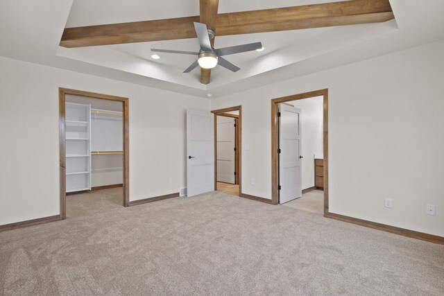 unfurnished bedroom featuring ceiling fan, a raised ceiling, a spacious closet, light carpet, and a closet