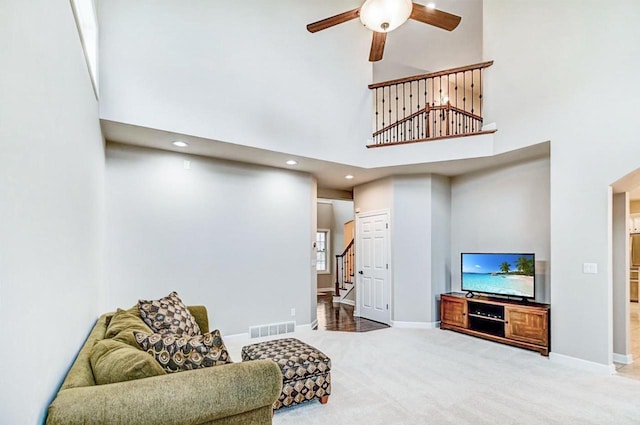 living room with a towering ceiling, ceiling fan, and carpet flooring