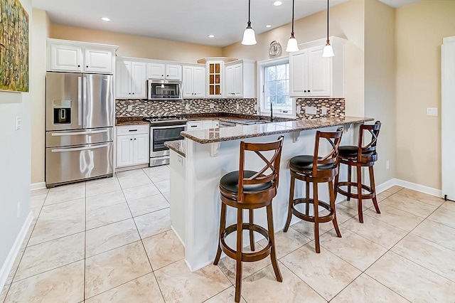 kitchen featuring pendant lighting, appliances with stainless steel finishes, dark stone countertops, white cabinets, and kitchen peninsula