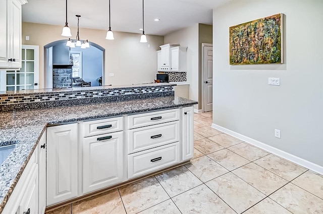 kitchen featuring tasteful backsplash, decorative light fixtures, dark stone countertops, light tile patterned floors, and white cabinets