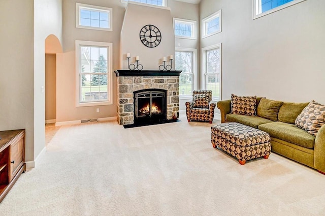 carpeted living room with a high ceiling, a stone fireplace, and a healthy amount of sunlight