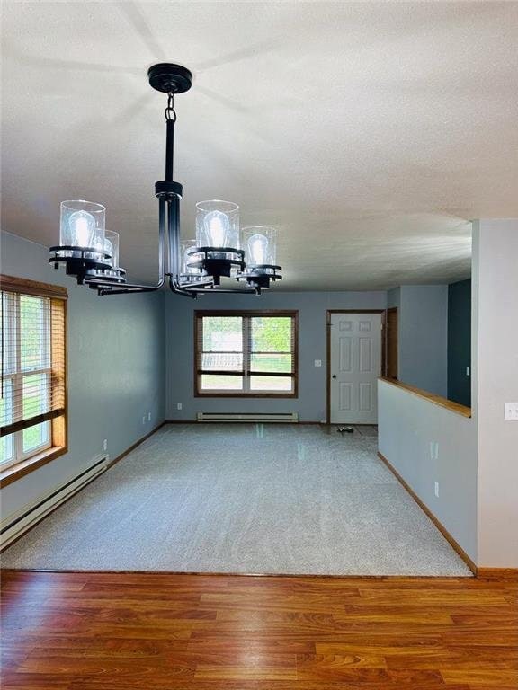 unfurnished living room with wood-type flooring, a baseboard radiator, and an inviting chandelier