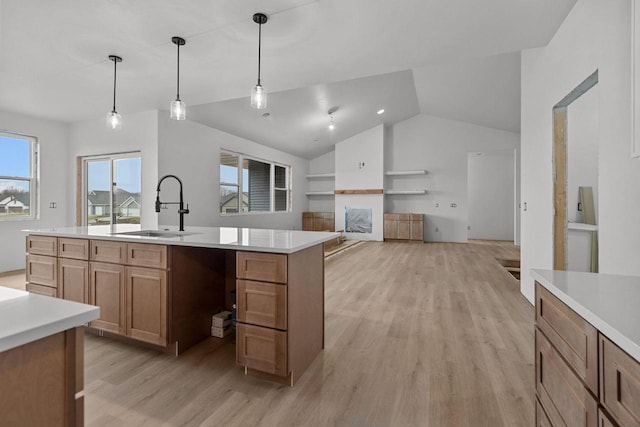 kitchen with lofted ceiling, sink, a kitchen island with sink, hanging light fixtures, and light hardwood / wood-style floors