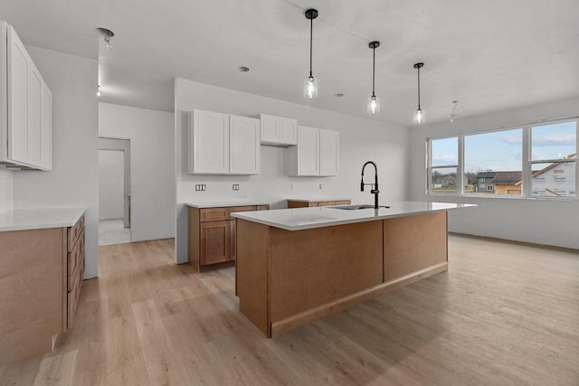 kitchen with sink, a kitchen island with sink, hanging light fixtures, white cabinets, and light wood-type flooring