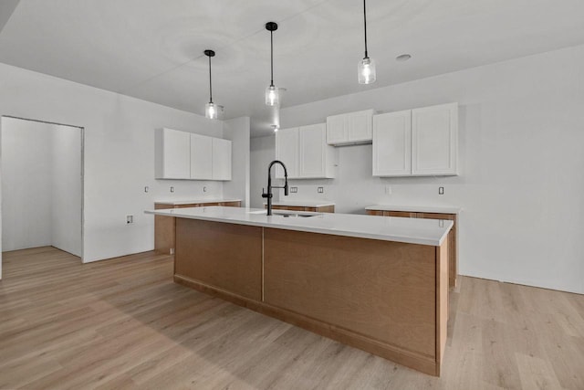 kitchen featuring pendant lighting, sink, white cabinets, and a center island with sink