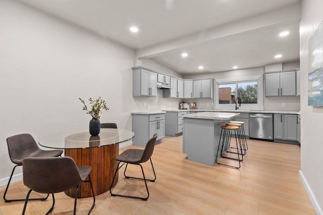 kitchen featuring gray cabinetry, stainless steel dishwasher, light hardwood / wood-style floors, a breakfast bar area, and a kitchen island