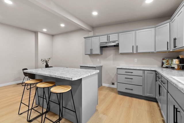 kitchen with a center island, light hardwood / wood-style flooring, beamed ceiling, gray cabinets, and a breakfast bar